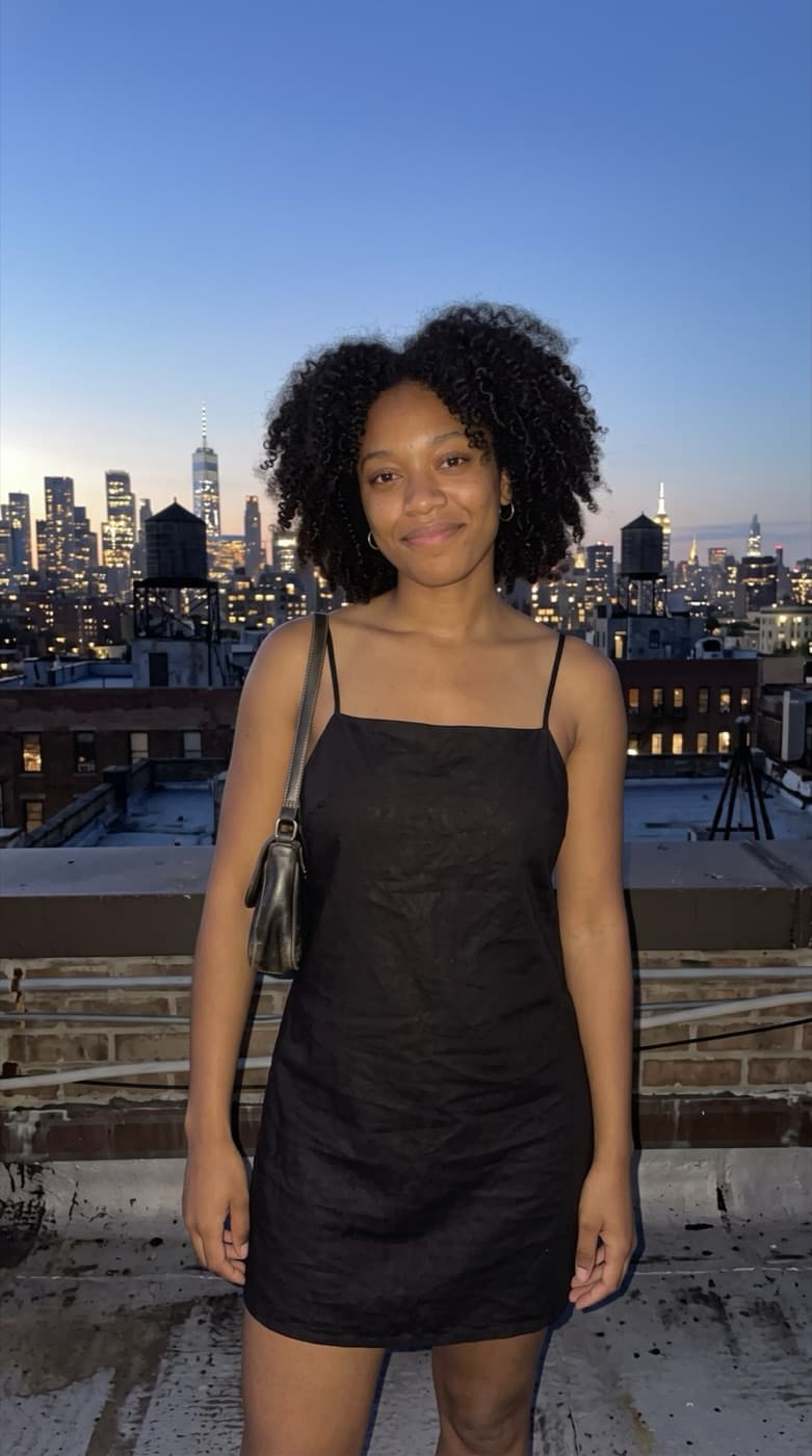 A woman in a black dress standing against a plain wall, with the NYC Rooftop look