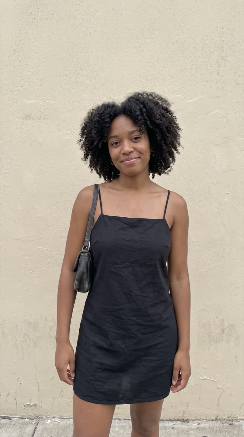 A woman in a black dress standing against a plain wall, original photo